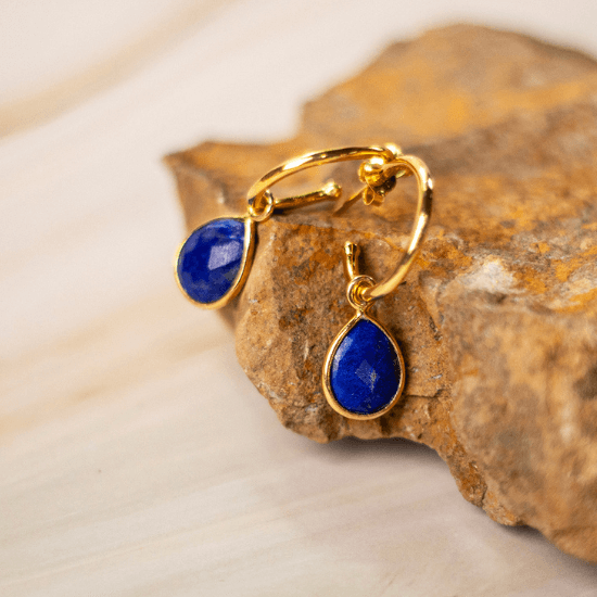 Gold vermeil hoop earrings with faceted teardrop-shaped lapis lazuli gemstones, displayed on a natural stone surface.