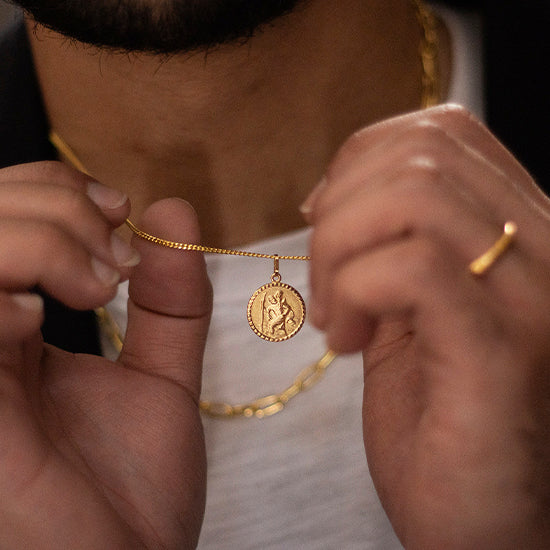 man holding a gold st Christopher necklace on a gold chain close up angle