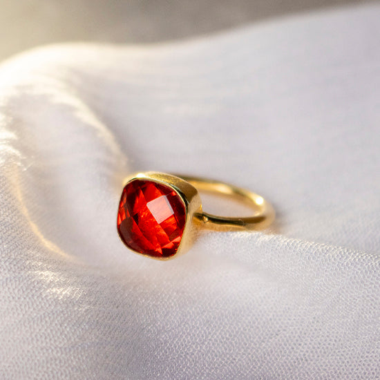 gold ring decorated with a large garnet gemstone lies on a piece of fabric 