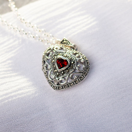 photograph of a heart shaped silver locket with a red garnet gemstone at its centre on a heavy silver chain