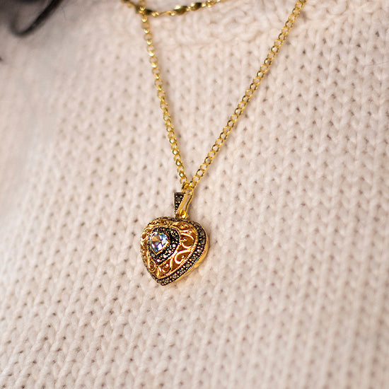 gold heart shaped locket with a blue topaz gemstone at its centre, worn by a woman