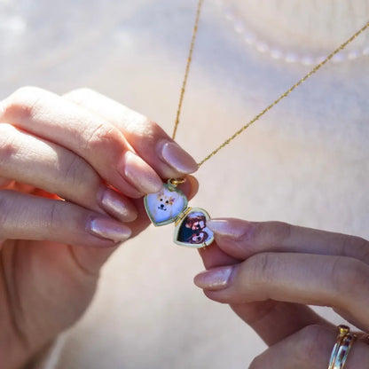 Close-up of a person holding an open gold heart-shaped locket necklace, revealing two small photos inside.