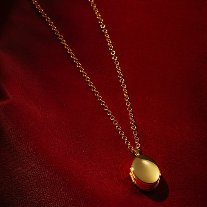 Gold oval locket necklace with a polished finish and chunky gold chain, displayed on rich red velvet fabric.