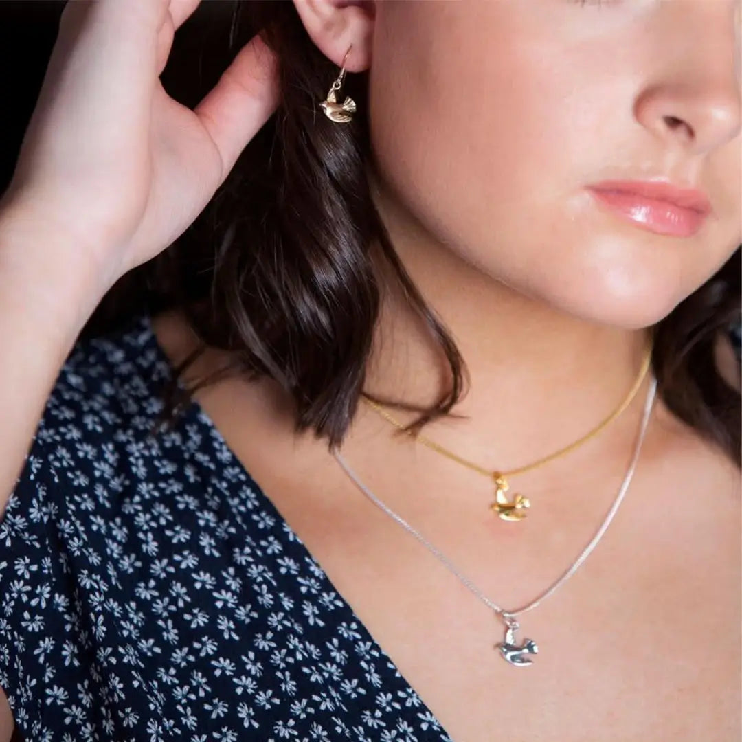 Gold bird charm earrings and layered necklaces in gold and silver, delicate everyday jewellery styling