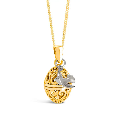Close-up of a gold filigree locket with decorative heart scrollwork and a small silver bird charm