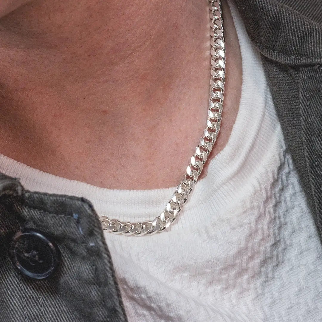 Close-up of a person wearing a sterling silver curb chain necklace styled with a white T-shirt and jacket