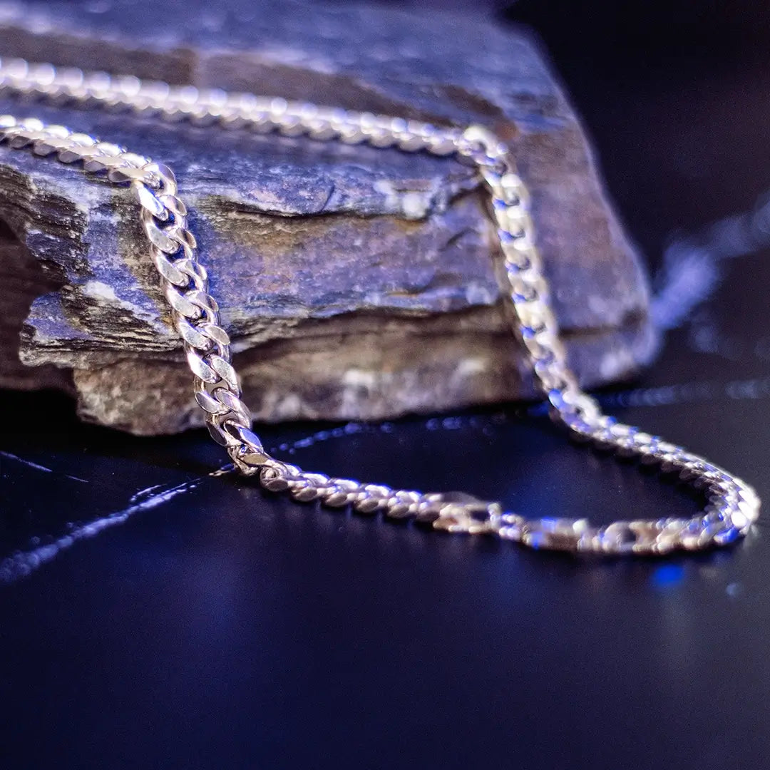 Sterling silver curb chain draped over a textured rock surface with soft blue lighting