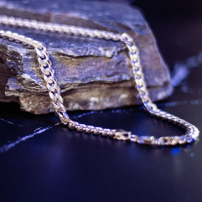 Sterling silver curb chain draped over a textured rock surface with soft blue lighting