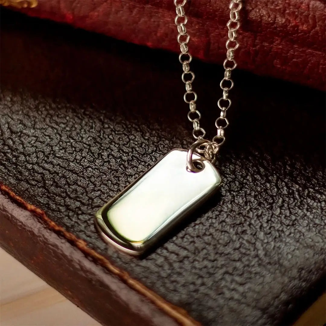 Sterling silver dog tag necklace on belcher chain resting on textured leather, polished blank pendant ready for engraving.