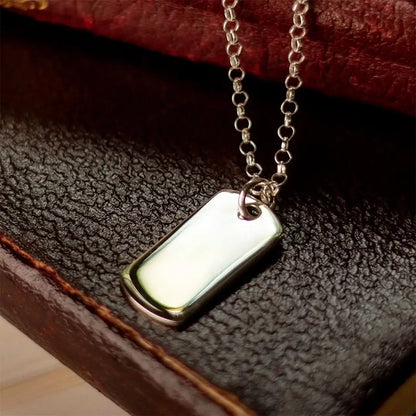 Sterling silver dog tag necklace on belcher chain resting on textured leather, polished blank pendant ready for engraving.