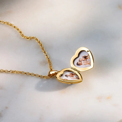 Open gold heart locket necklace showing two photo inserts on marble background