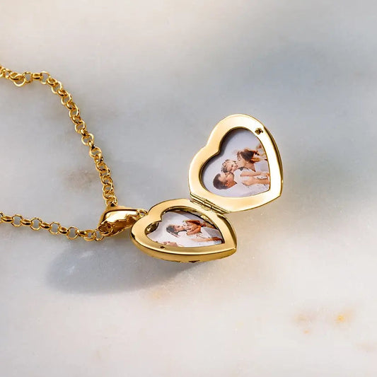 Open gold heart locket necklace showing two photo inserts on marble background