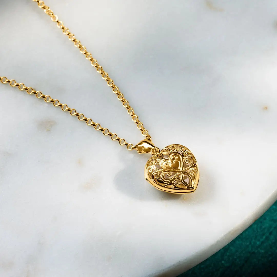 Gold filigree heart locket necklace on marble surface, intricate vintage-inspired design