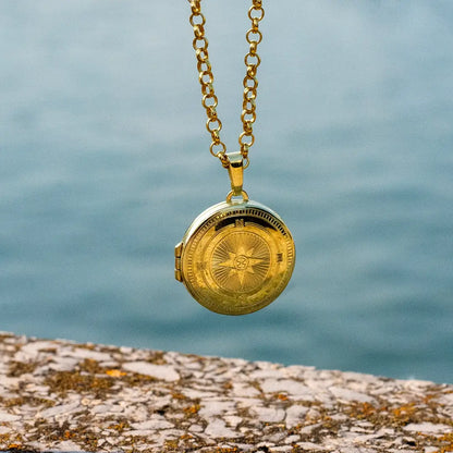 Gold compass locket necklace hanging outdoors above water, showcasing durability and polished finish