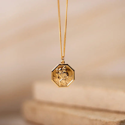 Gold hexagon St Christopher necklace suspended on fine chain against soft neutral background