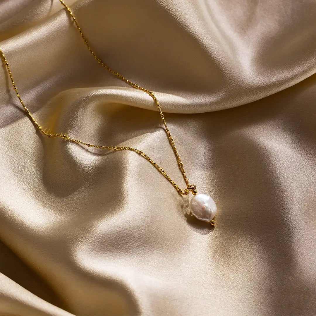 Gold coin pearl pendant necklace on gold satin fabric, highlighting natural freshwater pearl texture