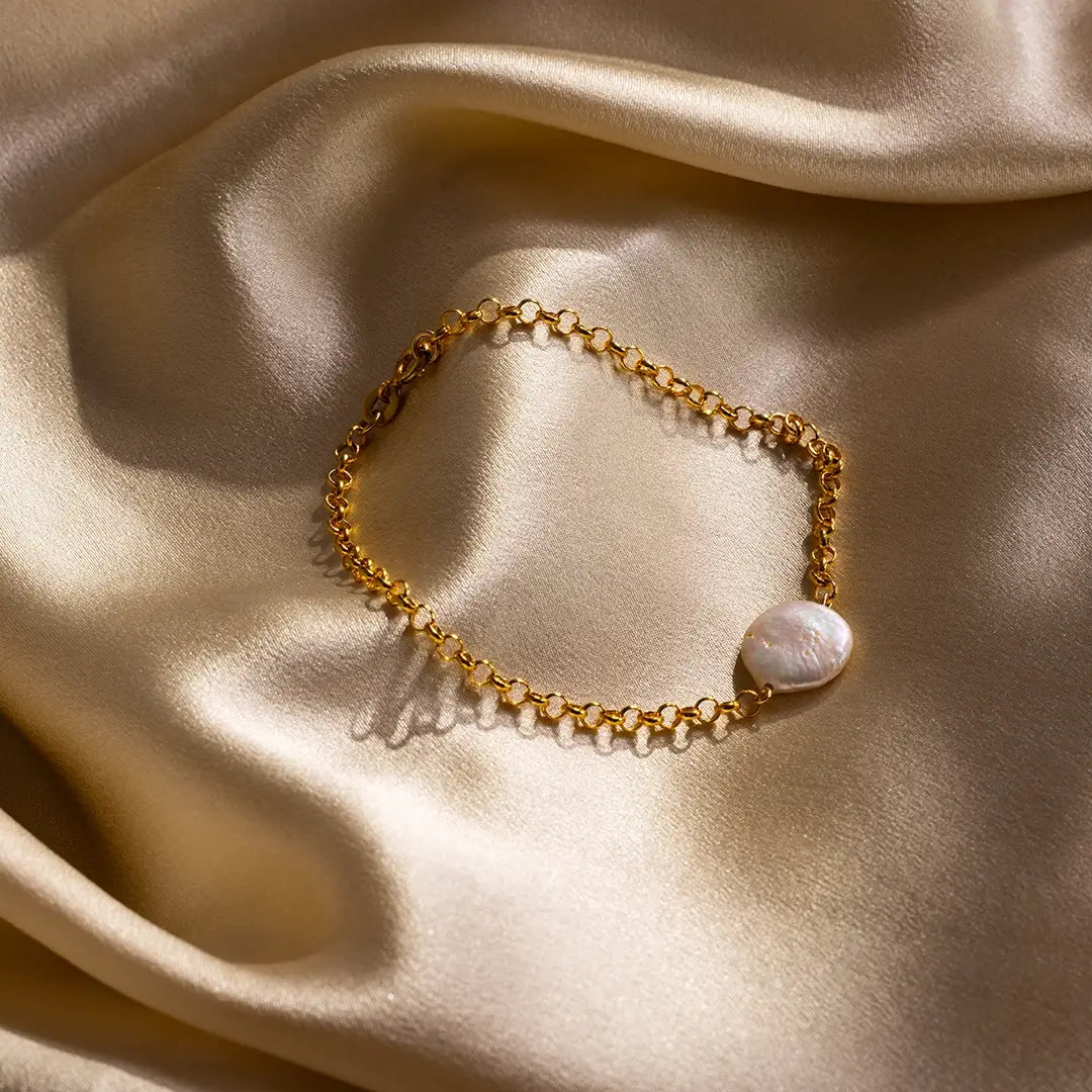 Gold coin pearl bracelet displayed on gold satin fabric, highlighting natural pearl lustre and texture