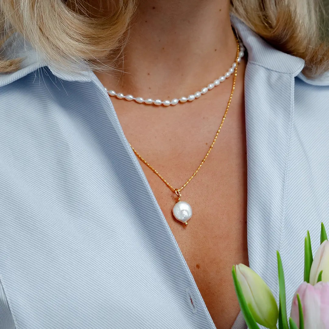 Close-up of gold coin pearl pendant necklace worn with pearl choker, highlighting natural pearl detail