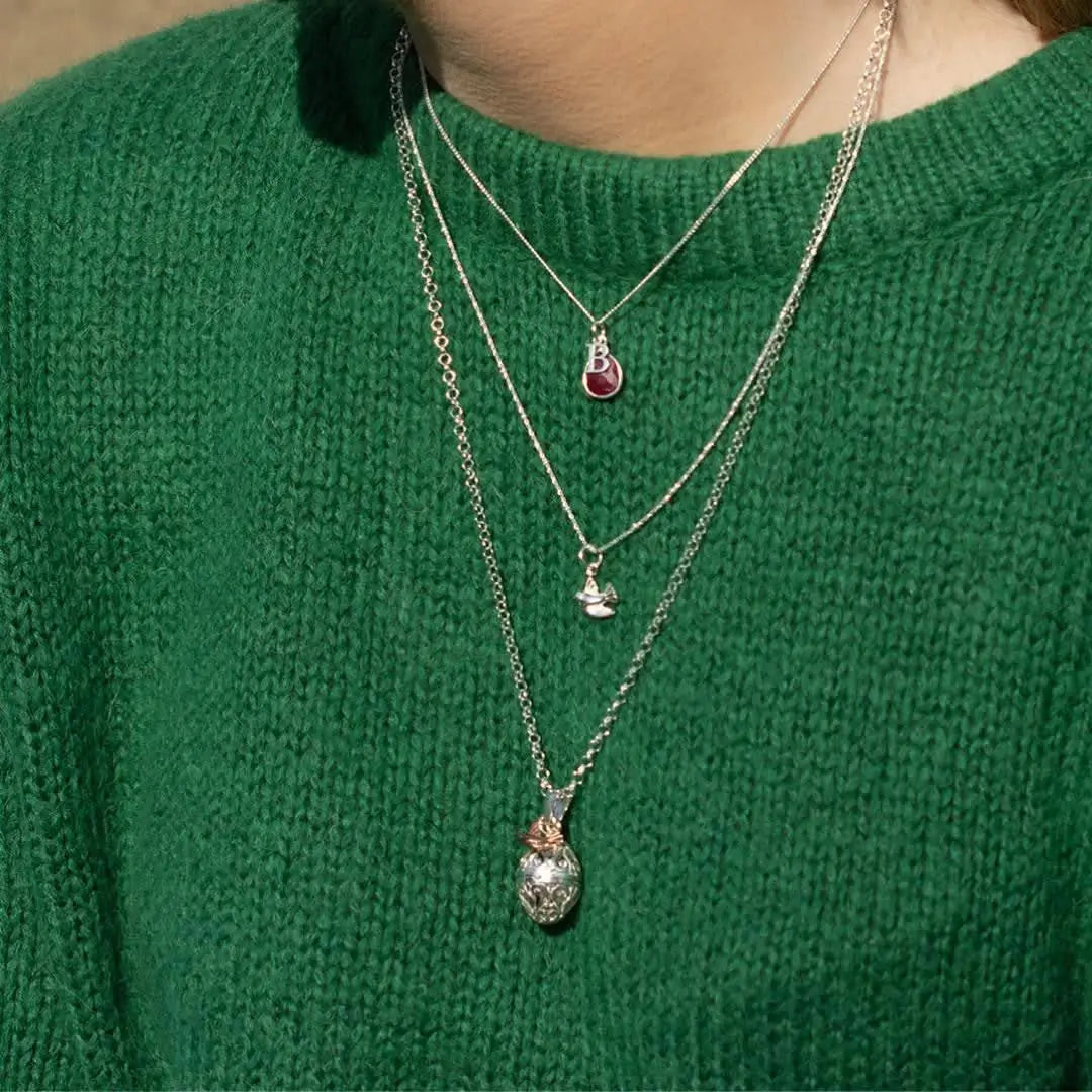 Sterling silver dove locket necklace layered with other chains on green jumper, meaningful personalised jewellery styling