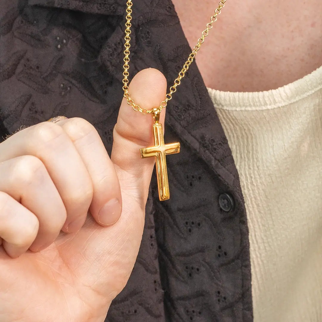 Close-up of a person holding a heavy polished gold cross necklace by Lily Blancheon a gold belcher chain