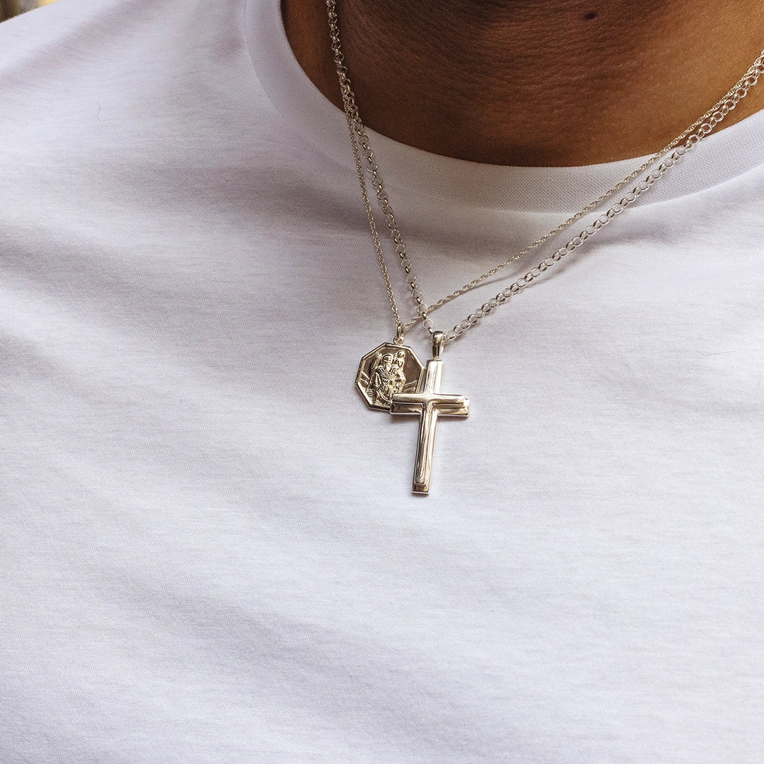 Sterling silver cross pendant necklace layered with St Christopher pendant on chains, worn by male model. By Lily Blanche.