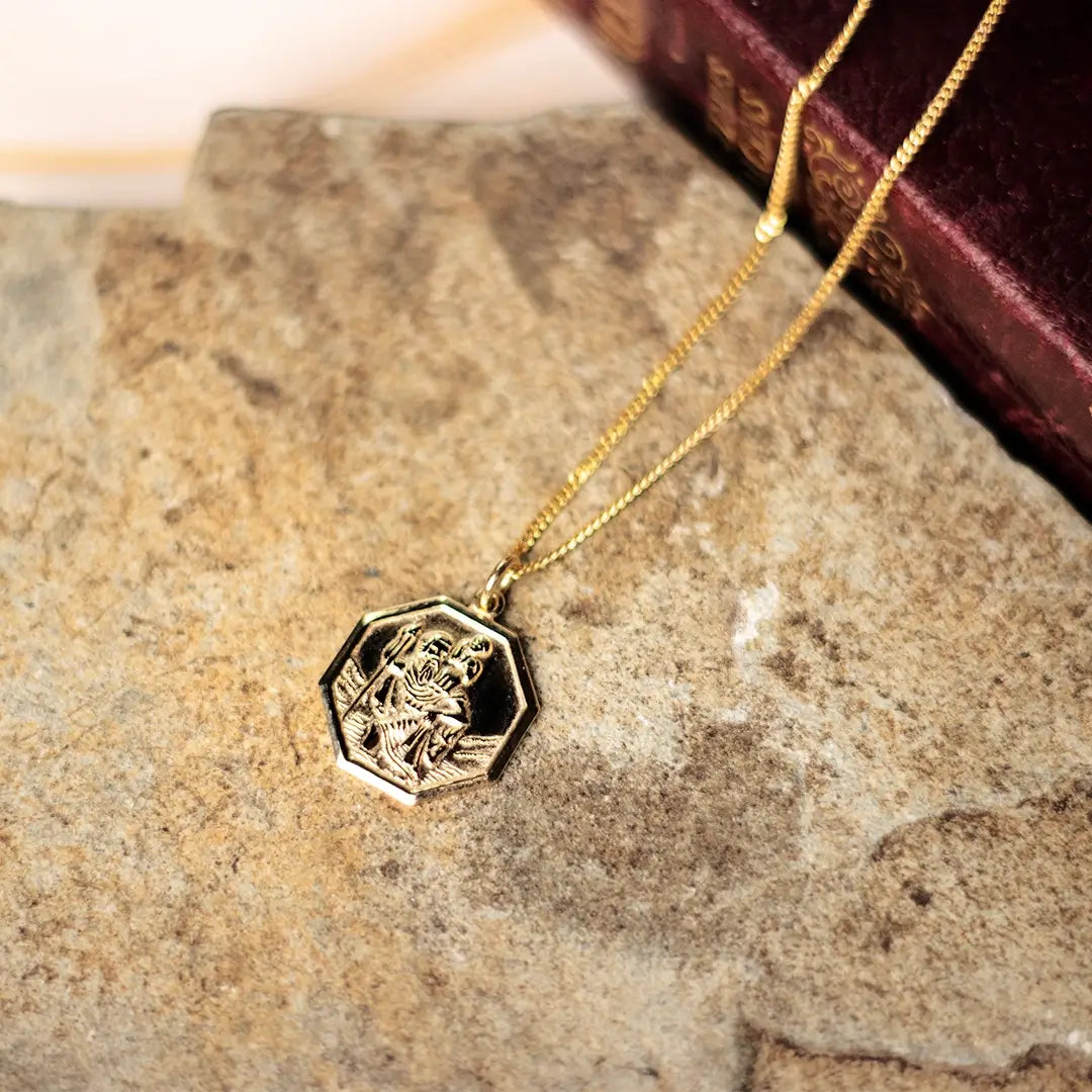 Gold hexagon St Christopher pendant necklace on natural stone surface, showcasing durability and shine