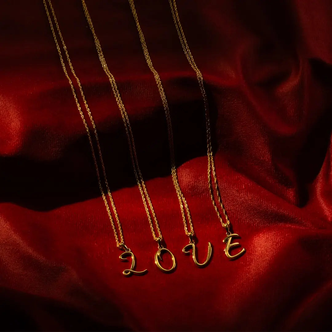 Solid gold initial necklaces spelling LOVE on fine chains, styled on red satin background