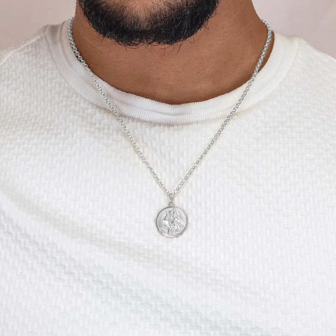 Close-up of a person wearing a sterling silver St Christopher coin pendant necklace on a belcher chain over a textured white top