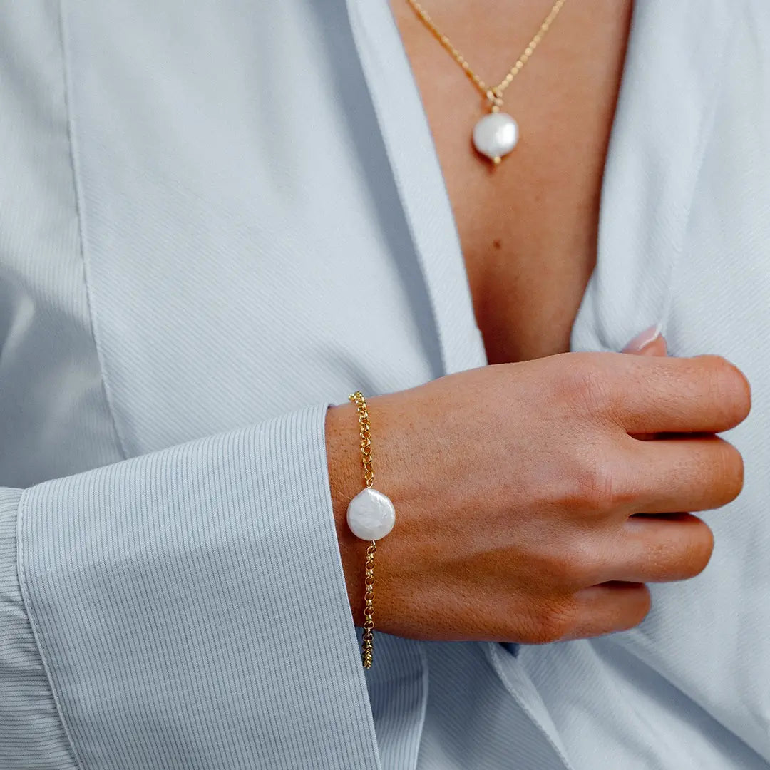 Close-up of woman wearing gold coin pearl bracelet and matching pendant necklace, layered pearl jewellery look