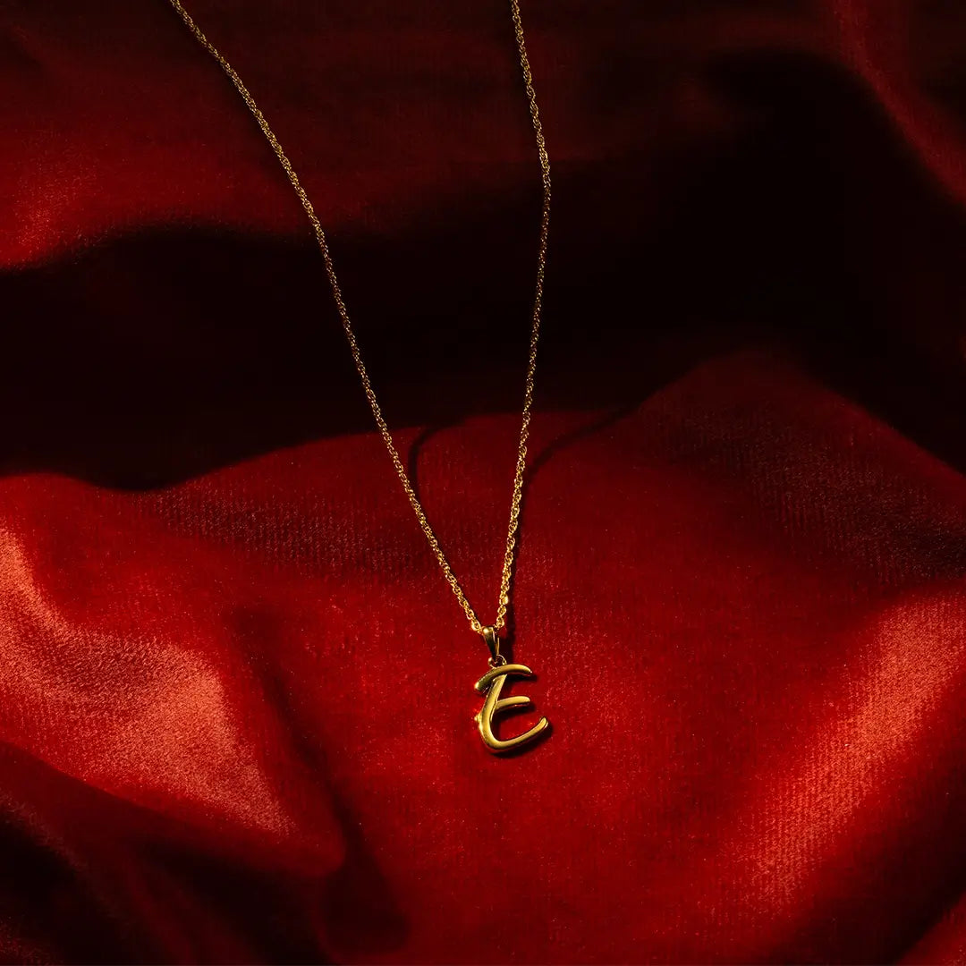 Solid gold initial E pendant necklace on fine chain, styled on red satin background