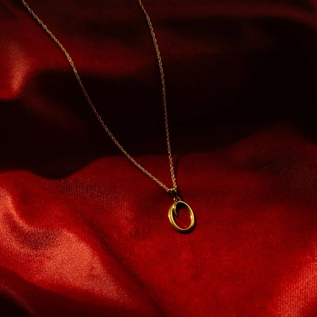 Solid gold initial O pendant necklace on fine chain, styled on red satin background