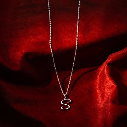 Sterling silver initial S pendant necklace on fine chain, styled on red satin background