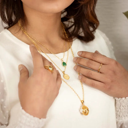 Woman wearing layered gold necklaces including a filigree bird locket pendant styled with gemstone and disc necklaces