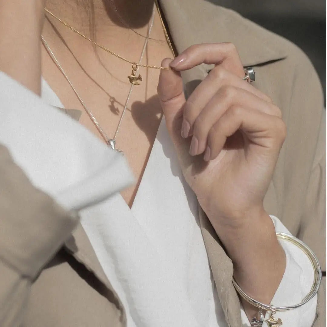 Gold bird charm necklace styled with layered chains, delicate everyday jewellery look