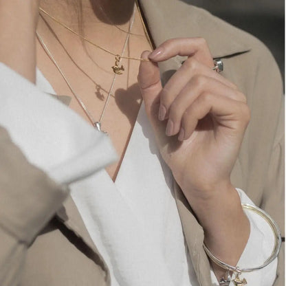 Gold bird charm necklace styled with layered chains, delicate everyday jewellery look
