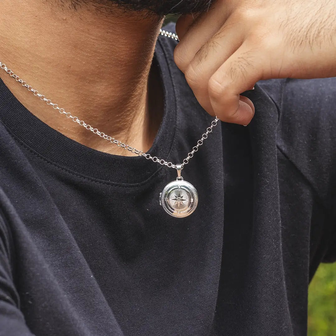 Close-up of a person wearing a silver compass locket necklace on a belcher chain, styled with a black t-shirt and jacket
