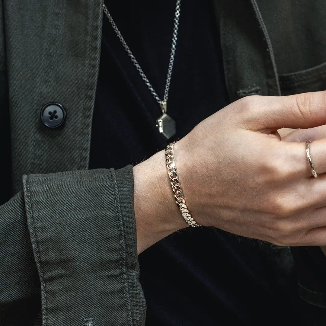 Close-up of men’s silver Cuban link bracelet worn on wrist with layered jewellery and dark outfit