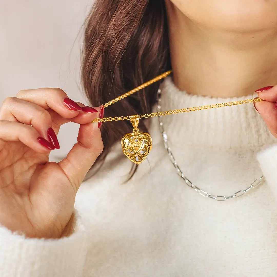 Woman holding gold filigree heart locket necklace, highlighting detailed craftsmanship