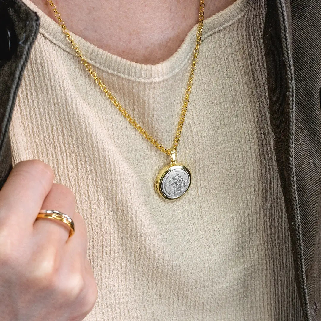 Close-up of a person wearing a gold St Christopher locket necklace with silver St Christopher emblem on a belcher chain