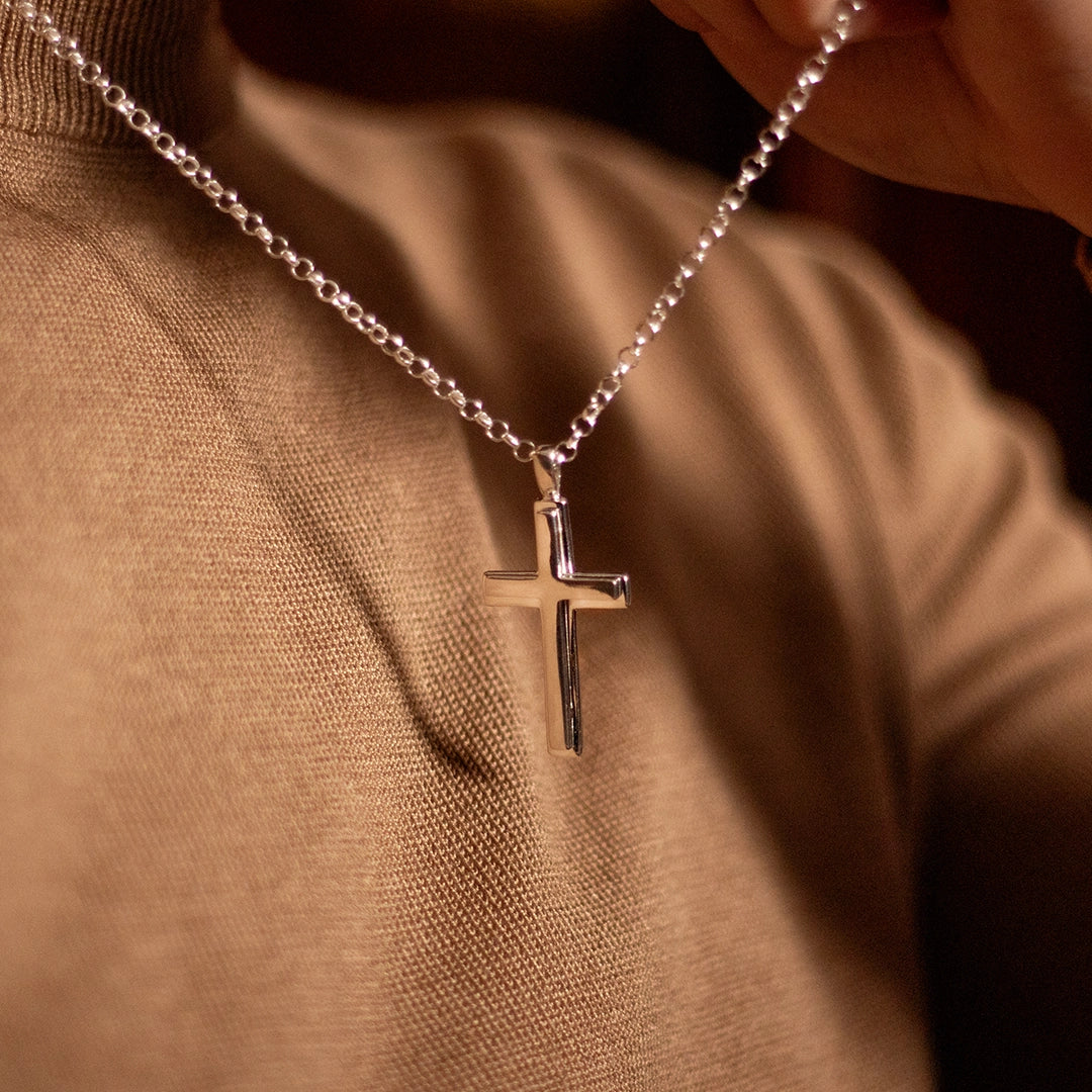 Sterling silver cross pendant necklace on chain, worn by male model in brown knitted top. By Lily Blanche.