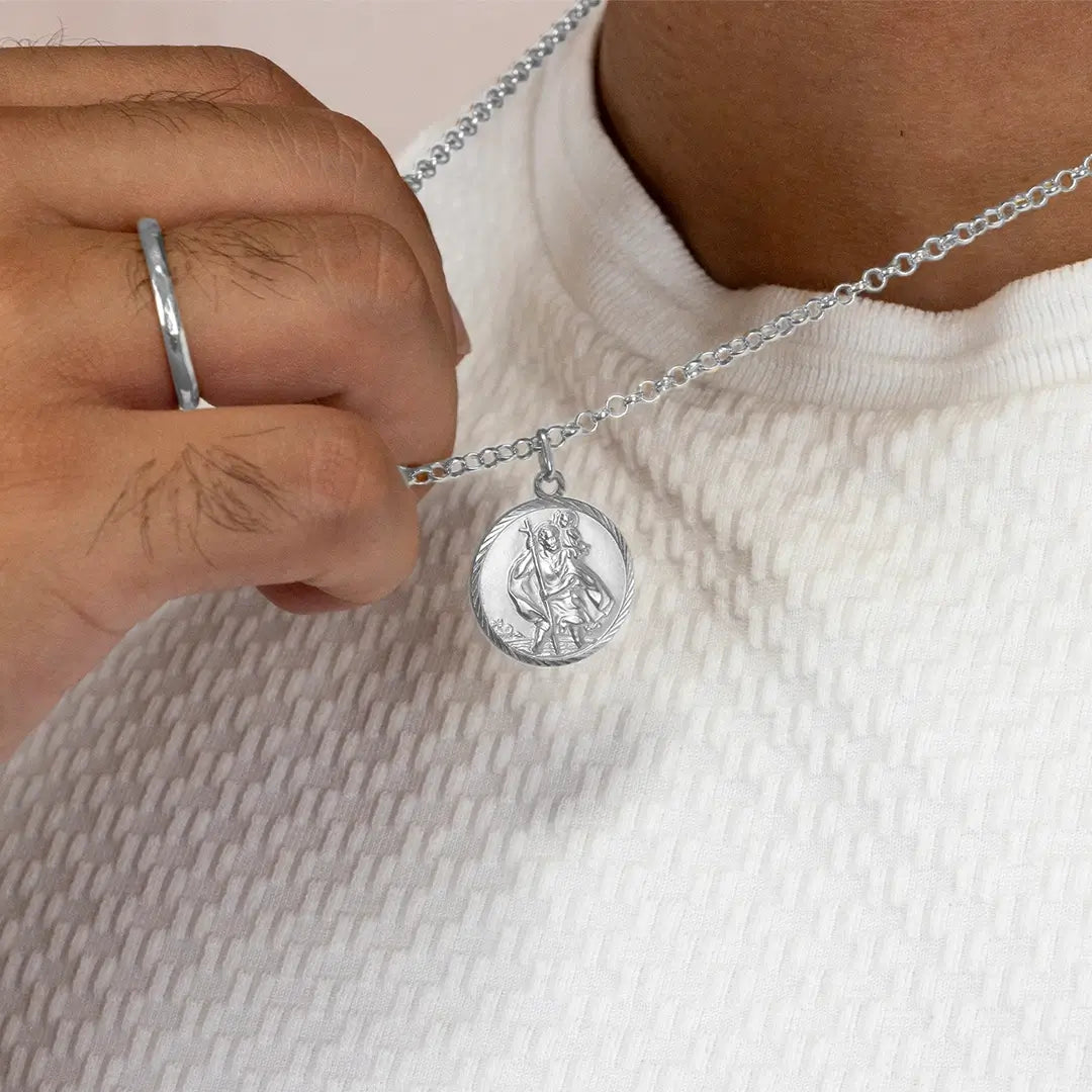 Close-up of a person holding a sterling silver St Christopher coin pendant necklace, highlighting the engraved front detail