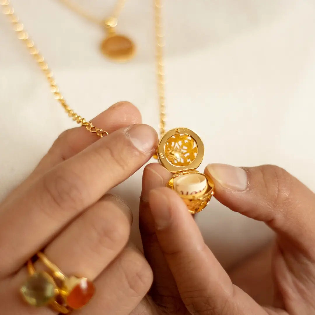 Close-up of hands opening a gold filigree locket revealing a rolled message inside