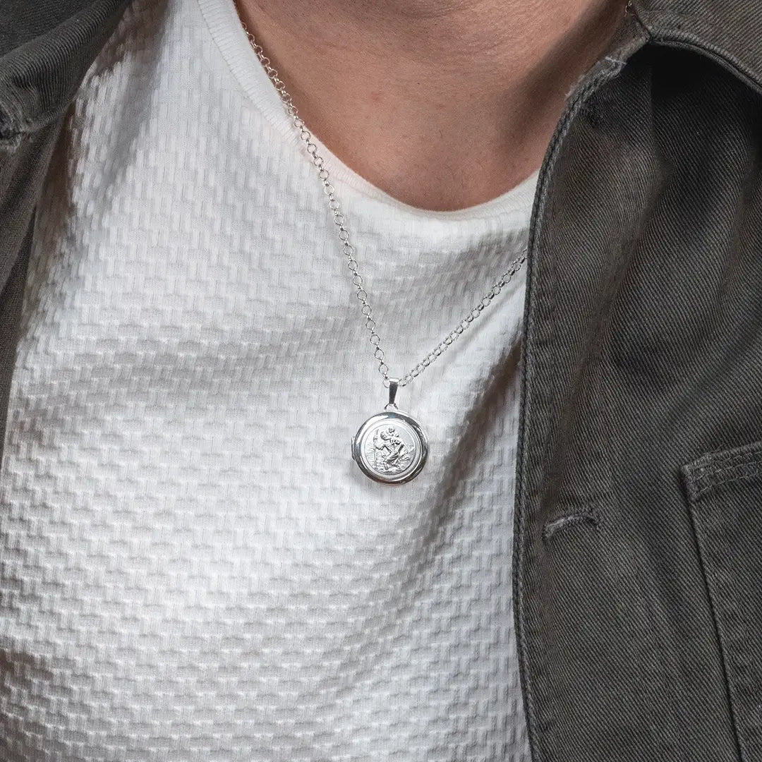 Person wearing a sterling silver St Christopher locket necklace on a fine chain over a white top and jacket