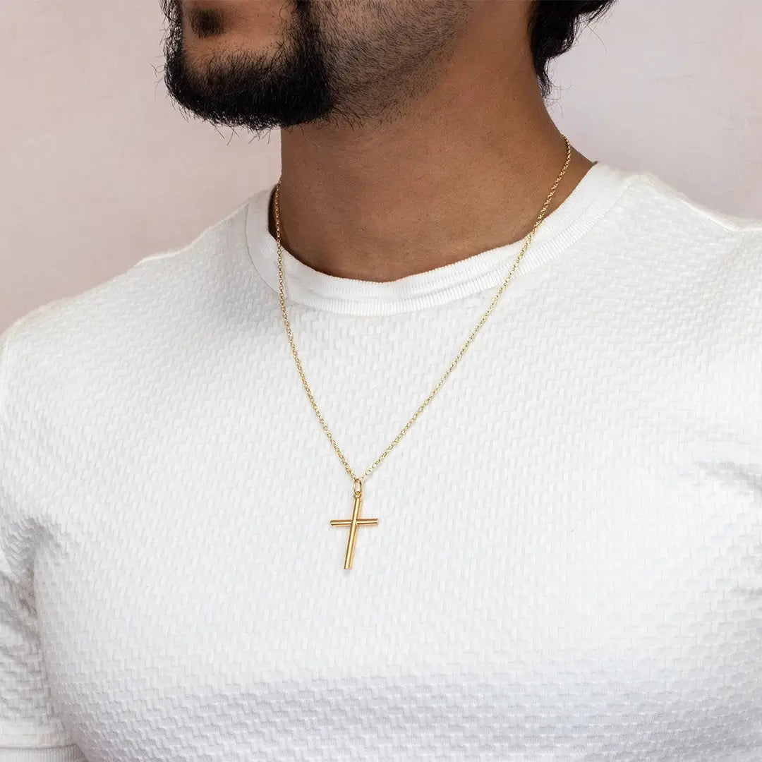 Close-up of a person wearing a gold cross necklace on a fine chain over a textured white top