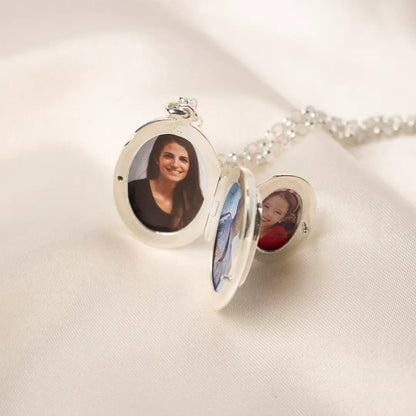 Open sterling silver oval locket necklace showing personalised photos inside, resting on soft cream fabric with delicate silver chain.