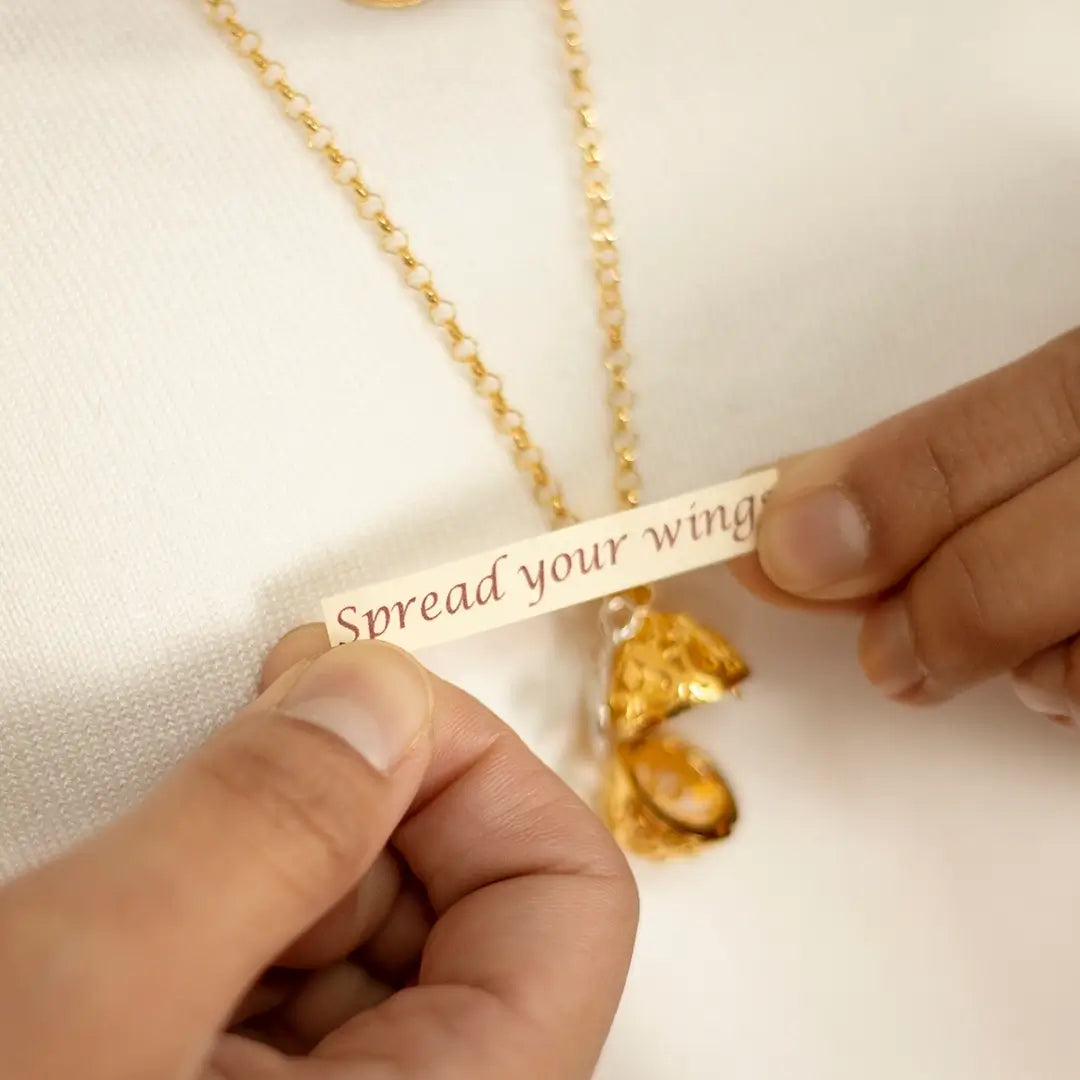Hands holding a small paper message reading “Spread your wings” removed from a gold bird locket