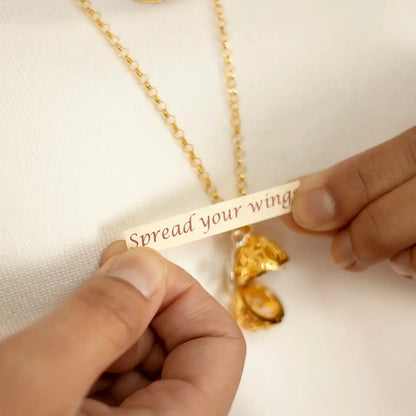 Hands holding a small paper message reading “Spread your wings” removed from a gold bird locket