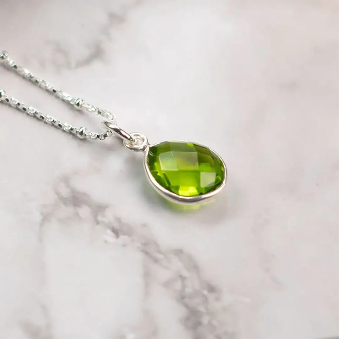 Sterling silver peridot teardrop pendant necklace on marble surface showing faceted green gemstone detail
