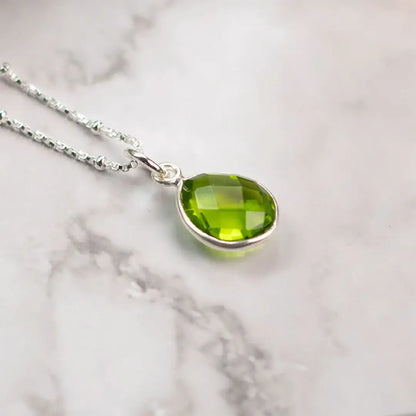 Sterling silver peridot teardrop pendant necklace on marble surface showing faceted green gemstone detail
