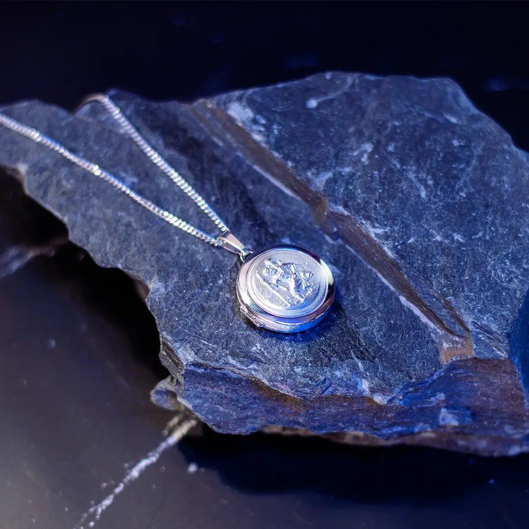 Sterling silver St Christopher locket necklace styled on natural rock with cool-toned lighting